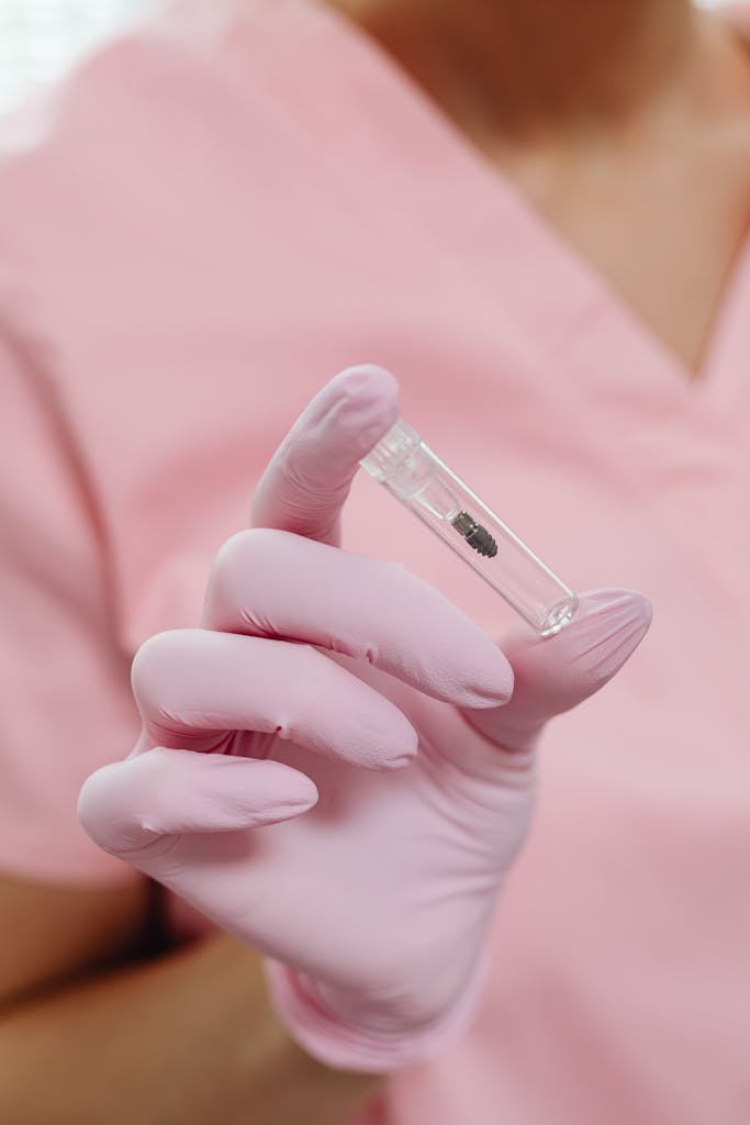 Close-up of a healthcare worker in pink uniform holding a medicine vial with gloved hands.